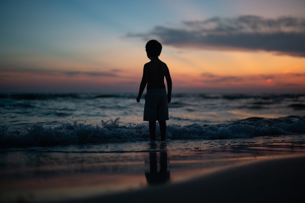 man in black shirt standing on seashore during sunset