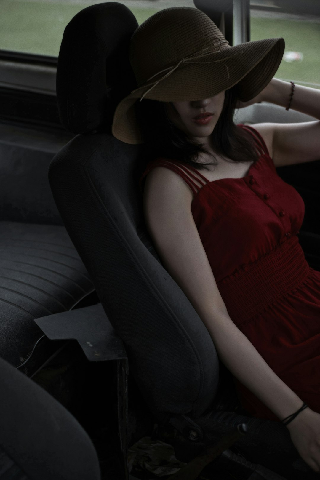 woman in red tank top and black pants wearing brown sun hat sitting on black car