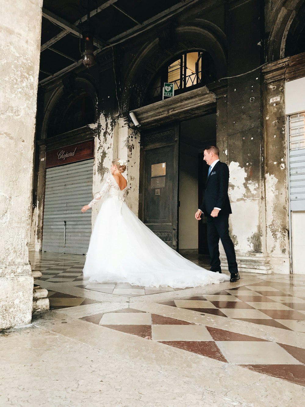 man in black suit and woman in white wedding dress walking on hallway