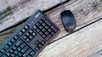 A black Logitech keyboard and mouse are placed on a wooden surface with visible grain and texture.