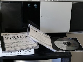 A Panasonic stereo system with a digital display indicating CD playing time next to a collection of classical music CDs featuring Strauss. One CD case is open, displaying the disc and cover booklet with musical notations.