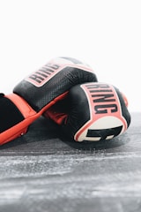 Close-up of rugged black wrestling gloves with red IronFury logo, resting next to a worn punching bag.