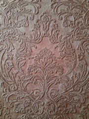An intricate, embossed pattern on a brown leather surface featuring ornate floral designs and swirling motifs. The detailed craftsmanship showcases symmetrical arrangements and delicate curves that give a textured and luxurious appearance.