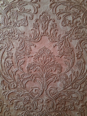 An intricate, embossed pattern on a brown leather surface featuring ornate floral designs and swirling motifs. The detailed craftsmanship showcases symmetrical arrangements and delicate curves that give a textured and luxurious appearance.