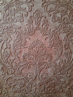 An intricate, embossed pattern on a brown leather surface featuring ornate floral designs and swirling motifs. The detailed craftsmanship showcases symmetrical arrangements and delicate curves that give a textured and luxurious appearance.