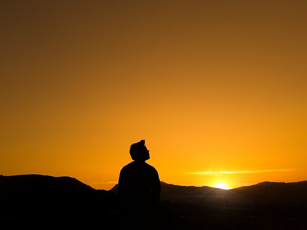 Silueta del hombre de pie en la colina durante la puesta del sol