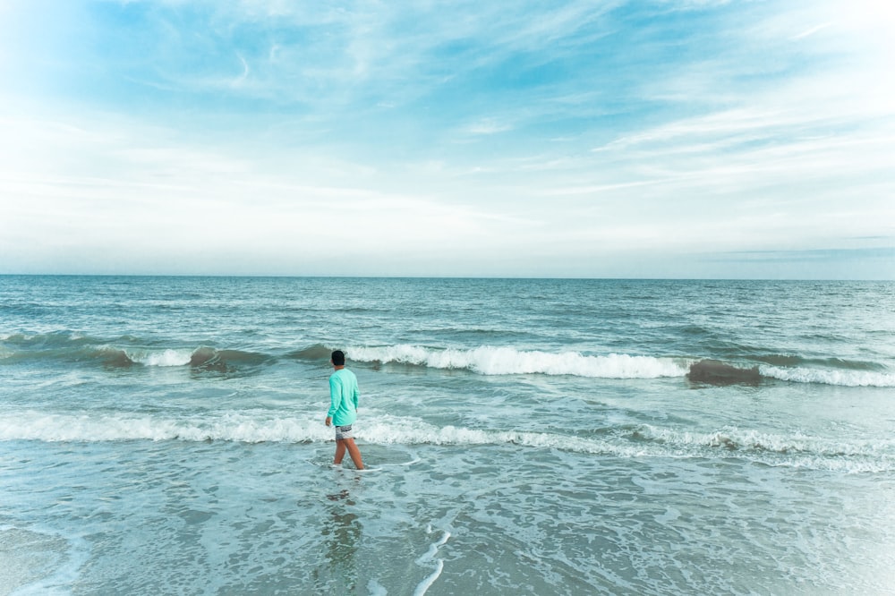 woman in blue shirt and red shorts standing on sea shore during daytime