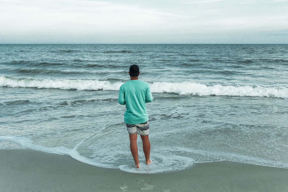 초록색 셔츠와 갈색 반바지를 입은 남자가 낮에 해변에 서 있다