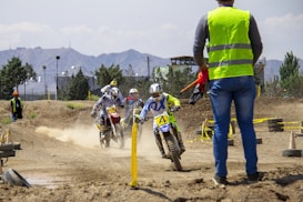 man in green and white jacket and blue denim jeans standing on dirt road during daytime
