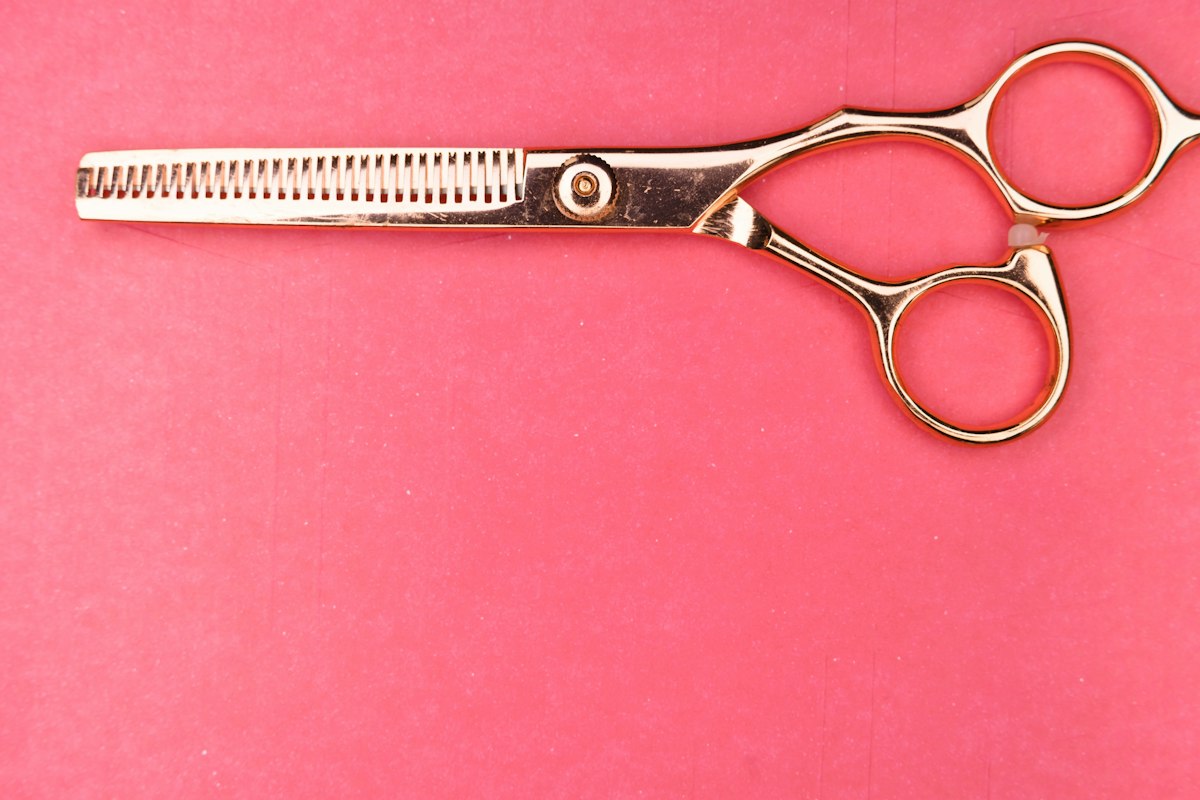 Gold-coloured hair thinning scissors lying on a pink background
