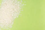 White rice grains are scattered over a bright green background, creating a contrast between the textures and colors.