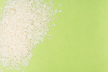 White rice grains are scattered over a bright green background, creating a contrast between the textures and colors.