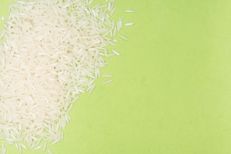 White rice grains are scattered over a bright green background, creating a contrast between the textures and colors.