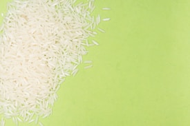 White rice grains are scattered over a bright green background, creating a contrast between the textures and colors.