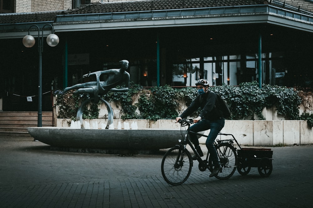 Hombre en chaqueta negra montando en bicicleta en la acera durante el día