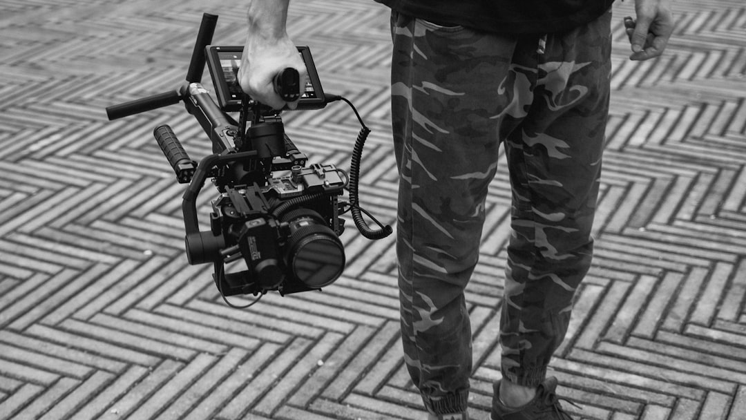 grayscale photo of man in camouflage pants holding dslr camera