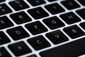 A close-up of a computer keyboard featuring black keys with white letters. The focus is on the middle row of keys including letters F, G, H, and others. The background and surrounding keys are blurred, highlighting the central keys.