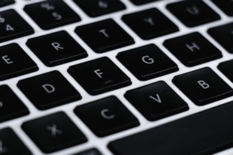 A close-up of a computer keyboard featuring black keys with white letters. The focus is on the middle row of keys including letters F, G, H, and others. The background and surrounding keys are blurred, highlighting the central keys.