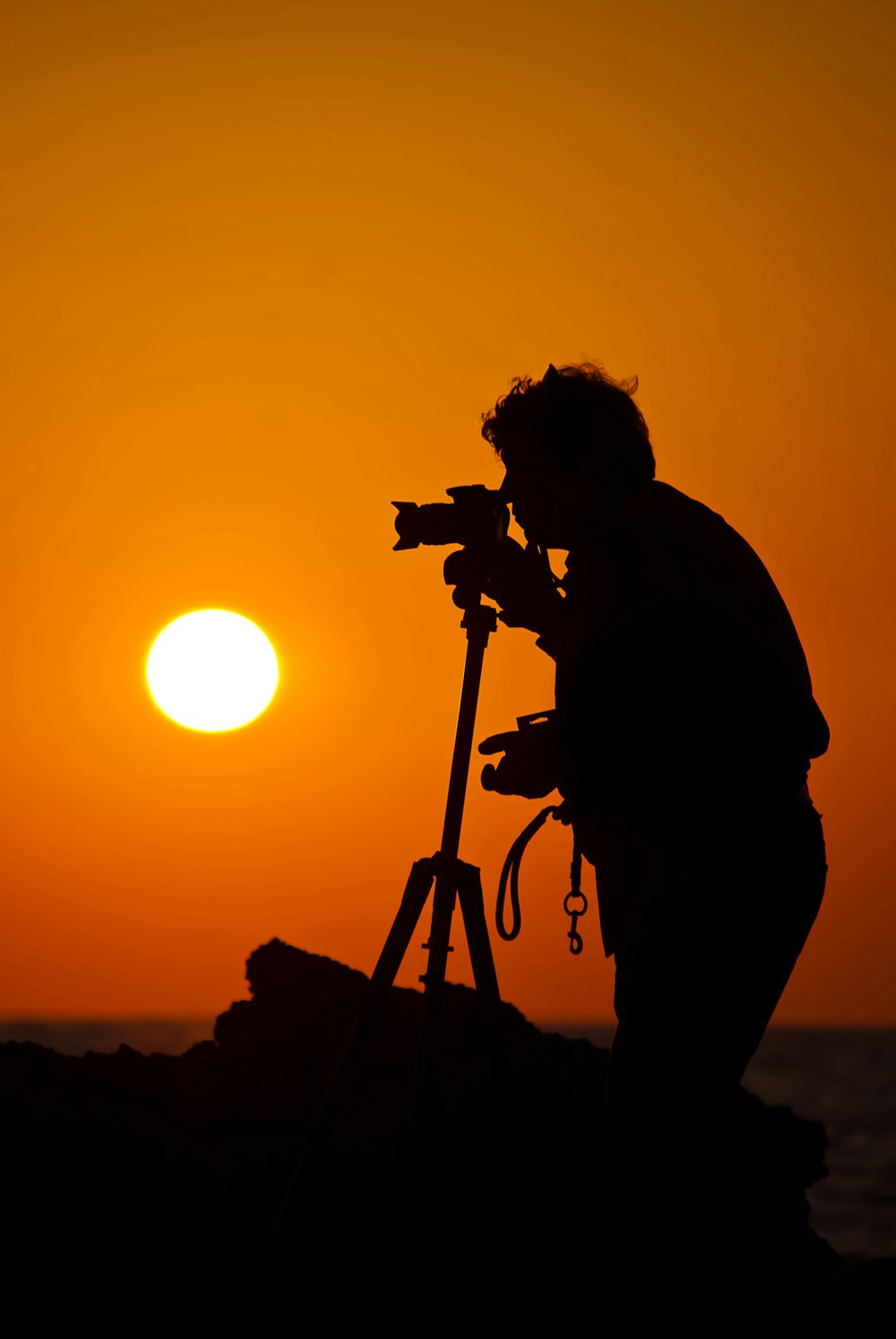 silhueta do homem em pé e segurando a câmera durante o pôr do sol