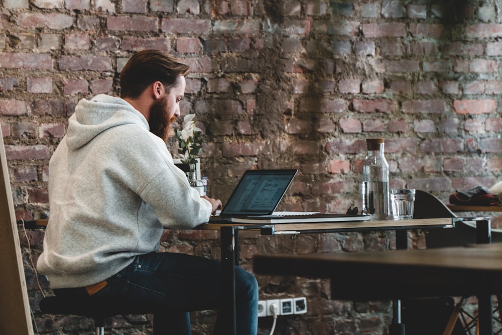 man in beige hoodie sitting on chair using laptop computer