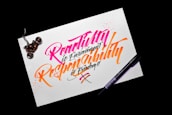 A piece of paper with colorful calligraphy reading 'Creativity is Contagious, Pass it on' written in vibrant pink and orange ink. The paper rests on a dark surface, with a black pen placed beside it. A motorcycle keychain sits on the top left corner of the paper.