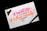 A piece of paper with colorful calligraphy reading 'Creativity is Contagious, Pass it on' written in vibrant pink and orange ink. The paper rests on a dark surface, with a black pen placed beside it. A motorcycle keychain sits on the top left corner of the paper.