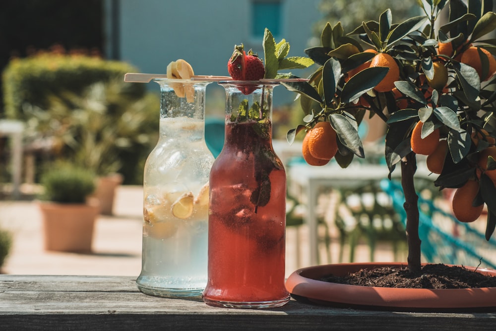 Botella de vidrio transparente con líquido rojo y limón sobre la mesa