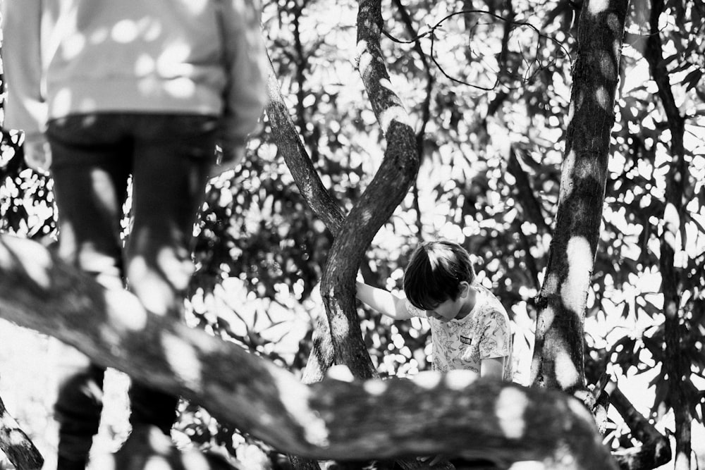 Foto en escala de grises de una chica con camisa blanca de pie debajo del árbol