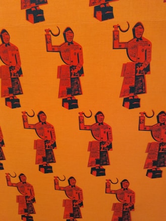 A repeated pattern of stylized figures resembling workers, holding a sickle in one hand. The figures are composed of collage-like elements with text and geometric shapes, set against an orange background. The design is minimalistic and graphic, using a limited color palette.