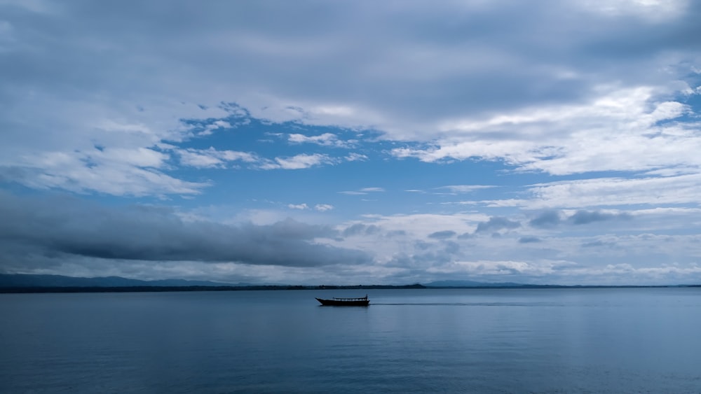 boat on sea under blue sky and white clouds during daytime