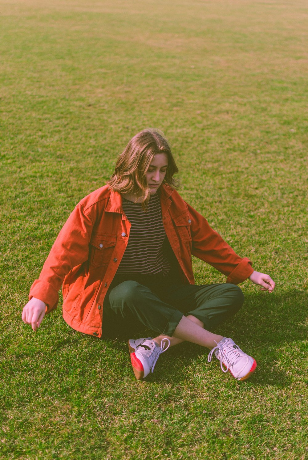 woman in red blazer sitting on green grass field during daytime