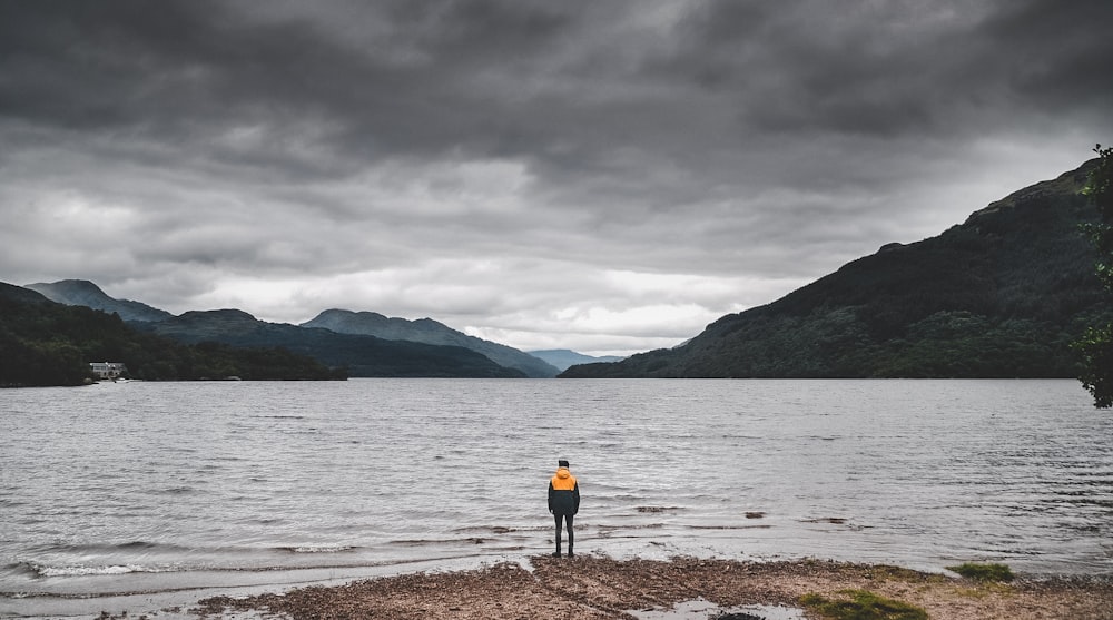 person in yellow jacket standing on brown sand near body of water during daytime