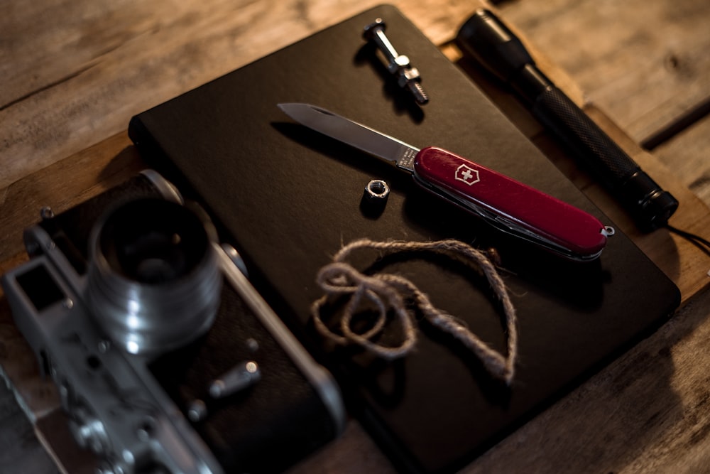 red and silver pocket knife beside black and silver camera lens