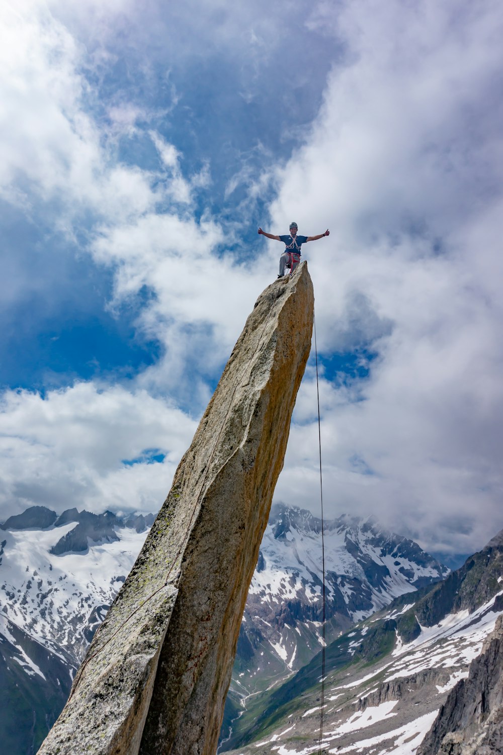 person in black jacket standing on brown rock formation under white clouds and blue sky during