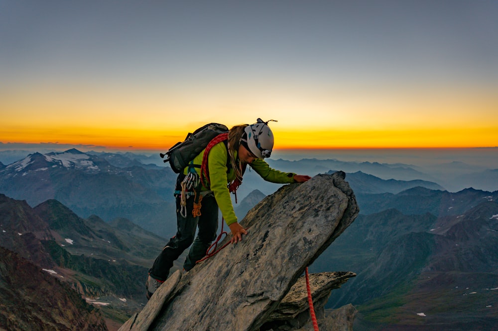 man in green jacket and black pants with black backpack standing on rock formation during daytime