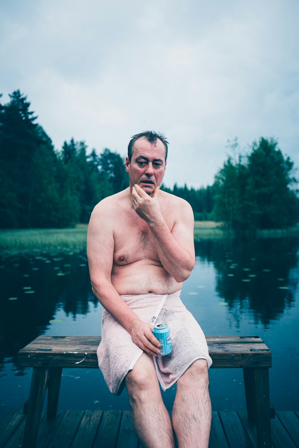 topless man sitting on brown wooden dock during daytime