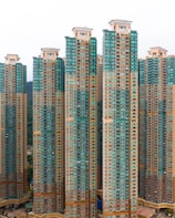 Tall residential skyscrapers with a modern design featuring a mix of teal and beige colors. The buildings have numerous windows and balconies, indicating high-density housing.