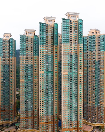 Tall residential skyscrapers with a modern design featuring a mix of teal and beige colors. The buildings have numerous windows and balconies, indicating high-density housing.