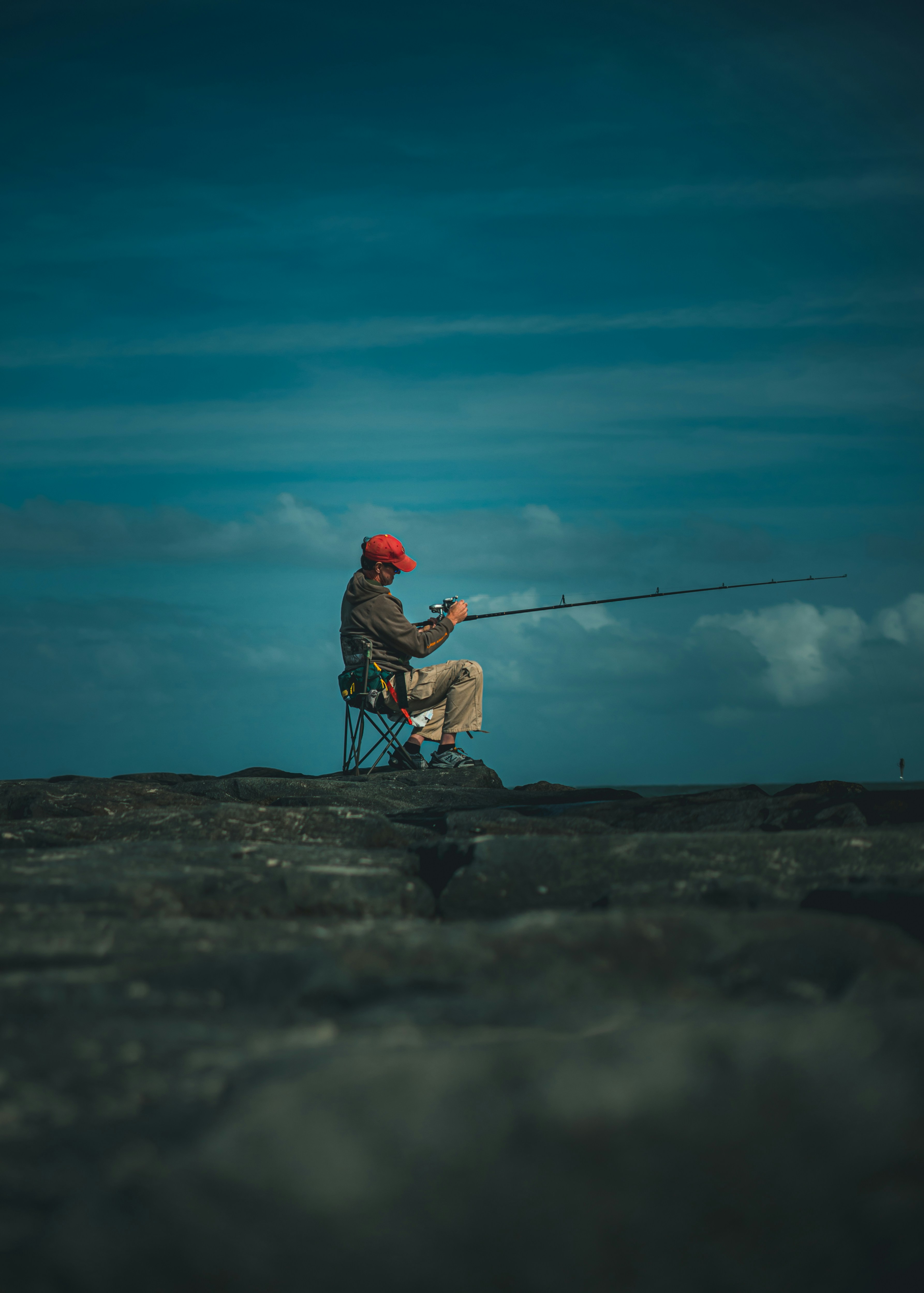 man in red hoodie and blue denim jeans fishing on sea during daytime