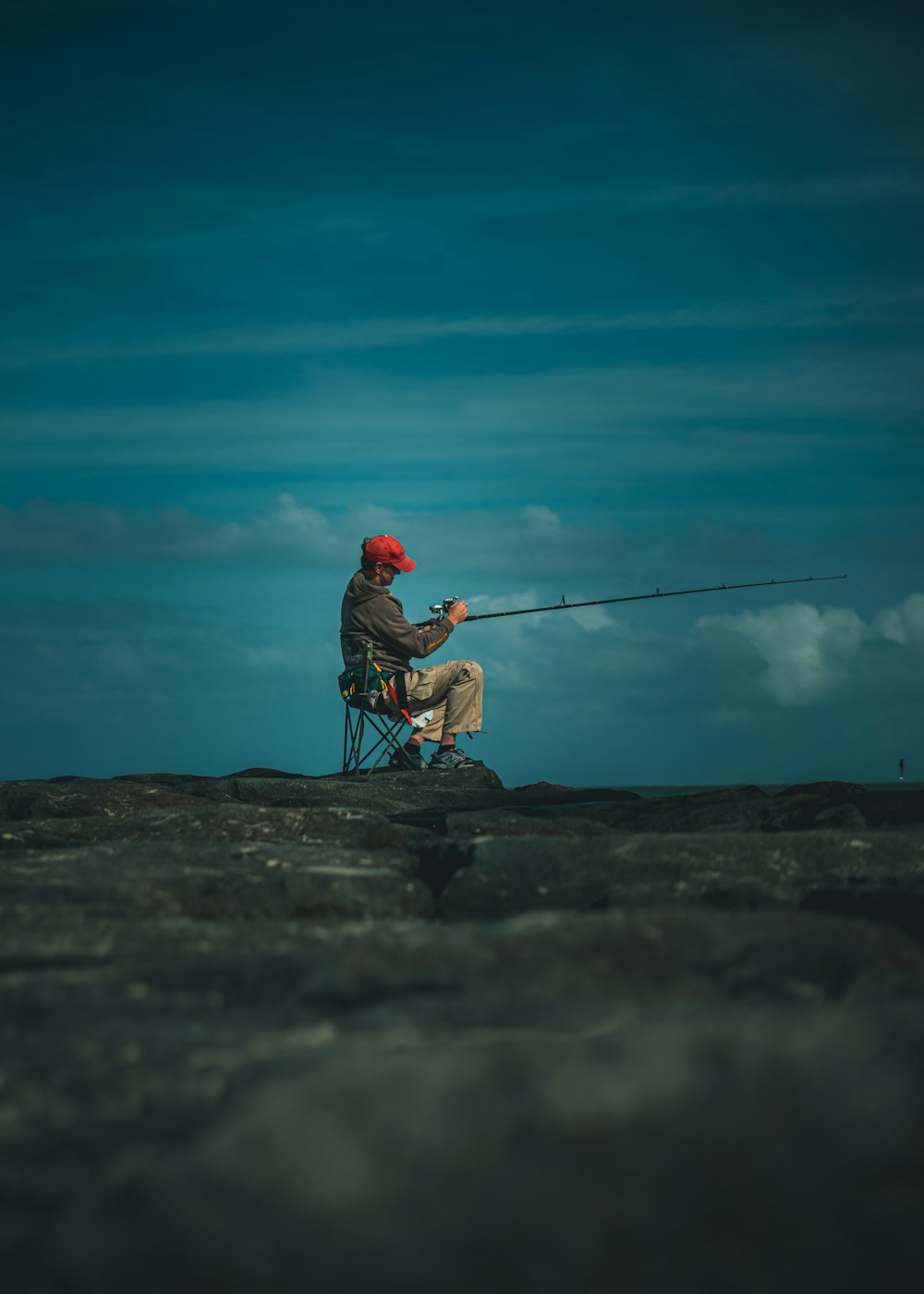 man in red hoodie and blue denim jeans fishing on sea during daytime