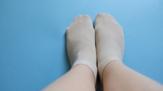 Close-up of feet in soft blue glacier socks resting on a plush sofa, showing contrast between cold feet and warm surroundings.