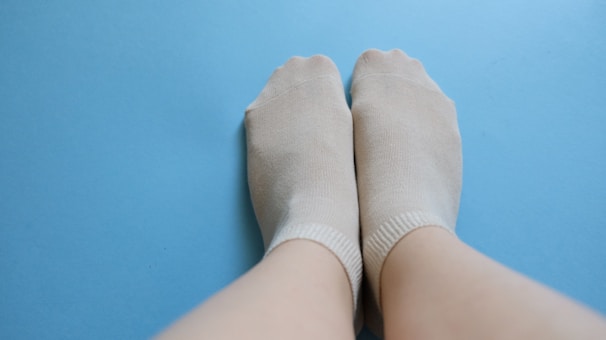 Close-up of feet in soft blue glacier socks resting on a plush sofa, showing contrast between cold feet and warm surroundings.