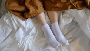 Feet wrapped in coral fleece slippers resting on a soft blanket beside a steaming cup of tea.