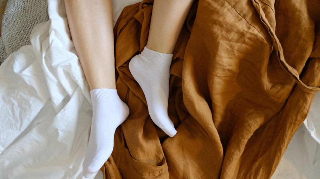 person wearing white socks on brown textile, Relaxed feet in basic, white socks on linen robe.