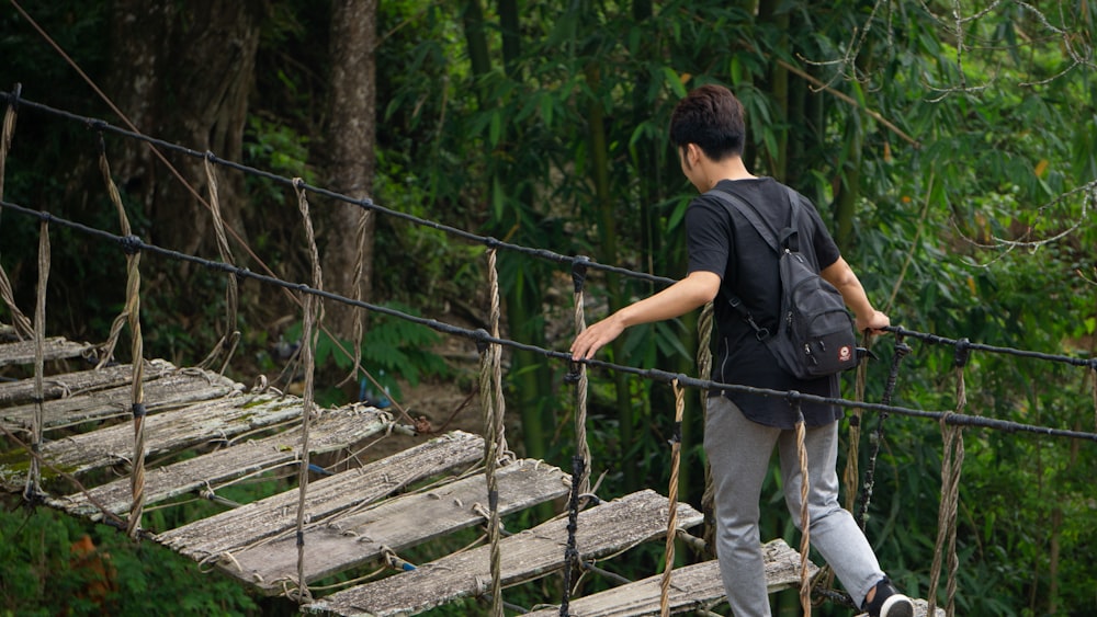 man in black t-shirt and blue denim jeans walking on wooden bridge