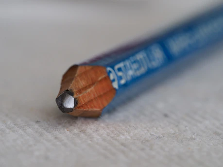 A close-up of a sharpened pencil resting on a textured wooden desk, with soft natural light highlighting its graphite tip.