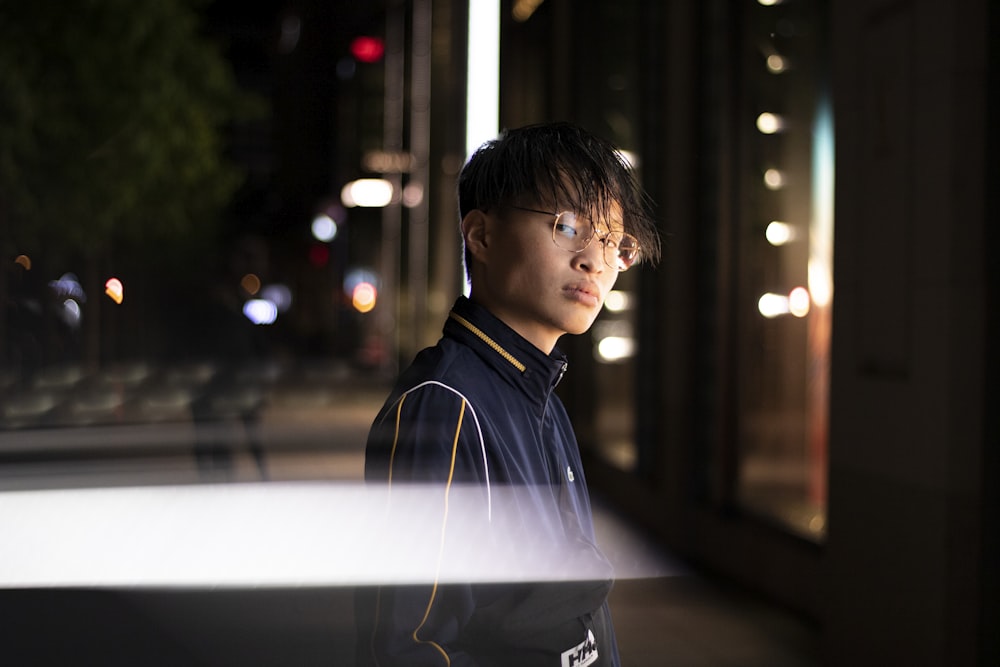 man in black leather jacket standing near building during night time