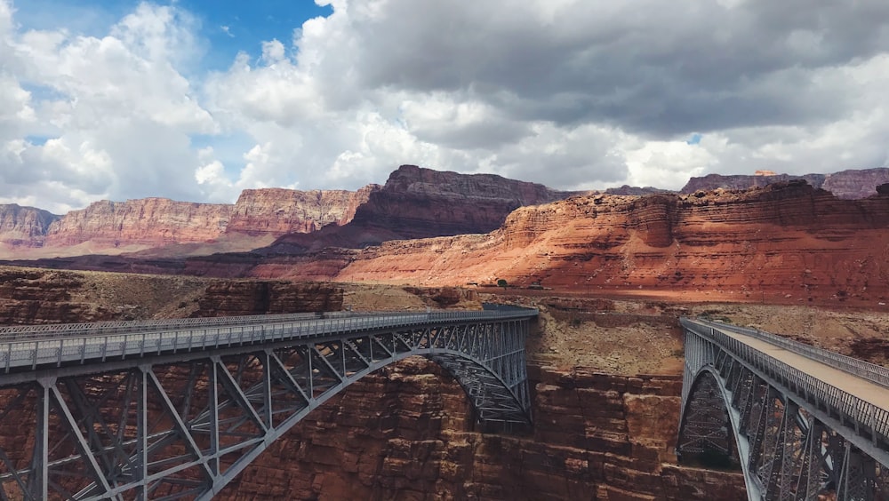 gray metal bridge over brown rocky mountain under white clouds and blue sky during daytime