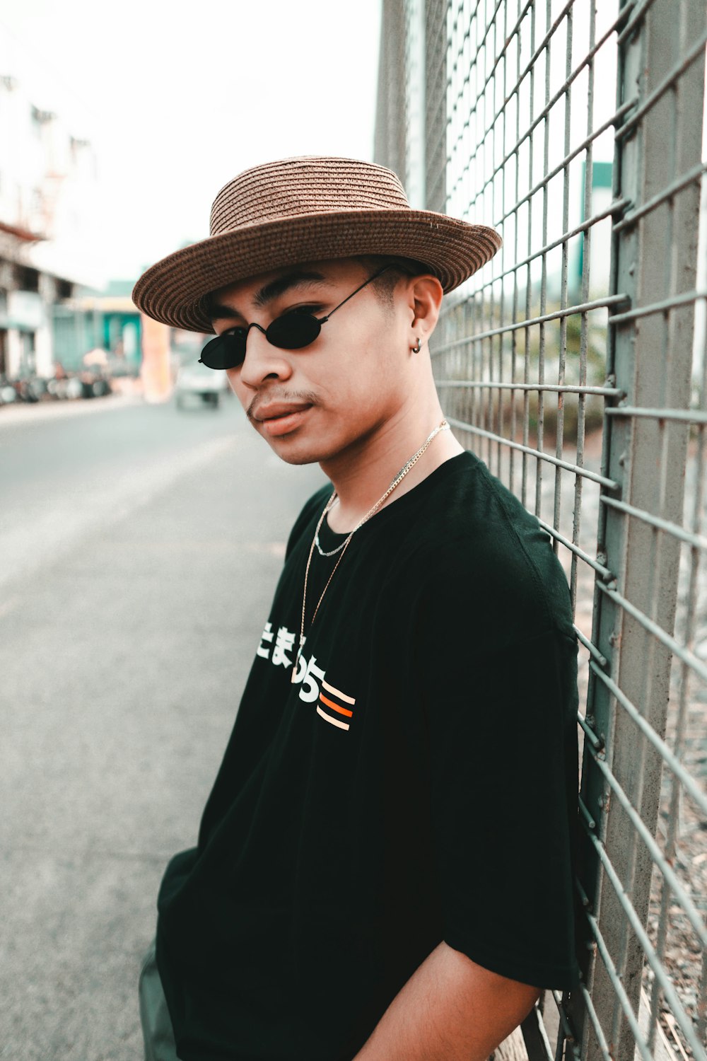 man in black crew neck shirt wearing brown fedora hat standing beside white metal fence during