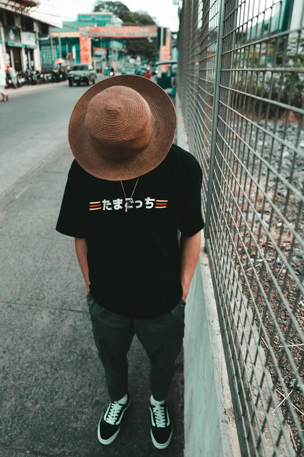 man in black t-shirt and brown hat standing on sidewalk during daytime